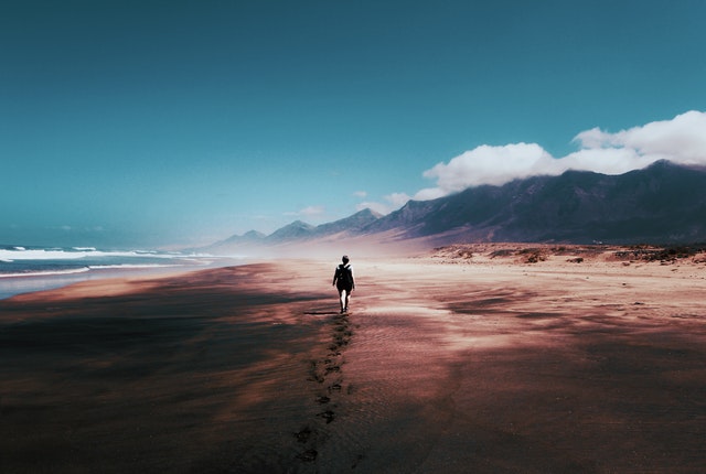 A child walking to the distant mountains on a long sandy beach. Show Don't Tell.
