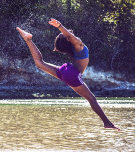 A beautiful African American woman in balletic pose leaping into a scenic river. Overcoming Writers Block